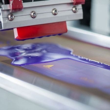 Nahaufnahme einer Siebdruckmaschine, die leuchtend violette Farbe auf ein Substrat aufträgt